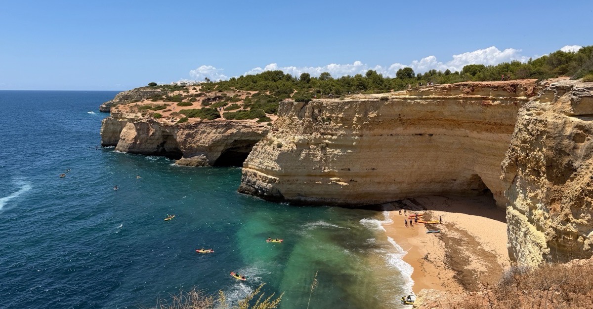 Limestone cliffs on the Algarve coast with kayakers paddling below in clear turquoise water