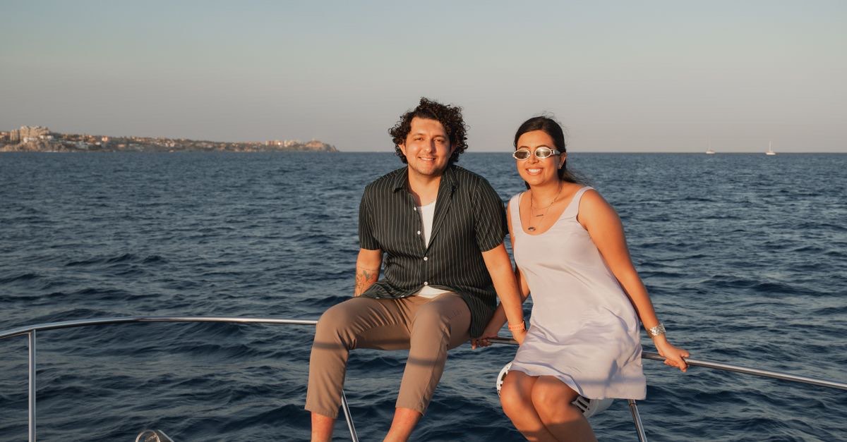 A couple sitting on the bow of a yacht looking out over the open sea