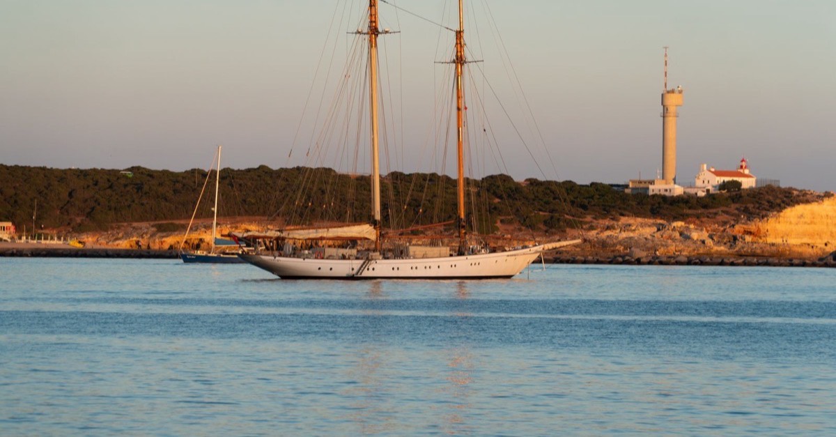 A two-masted schooner lying in evening light in front of the Ponta do Altar lighthouse at the river mouth
