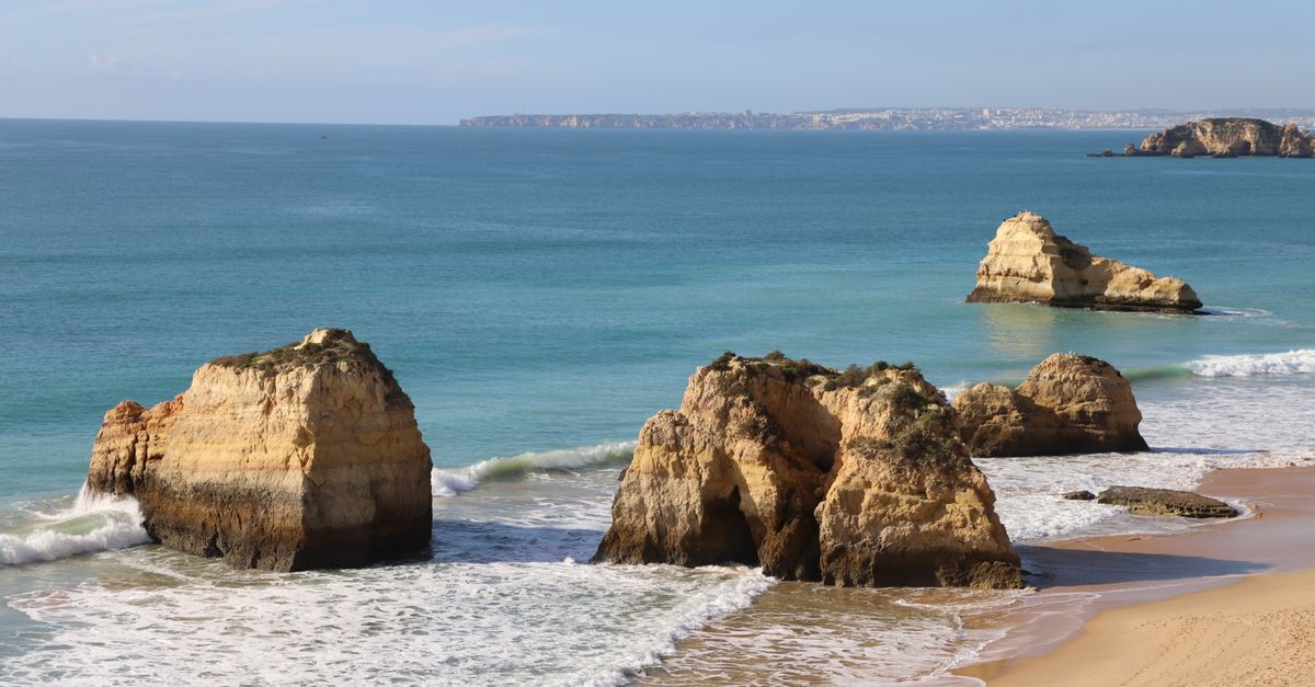Wide sandy beach with ochre rock stacks and turquoise water on the southern coast of Portugal