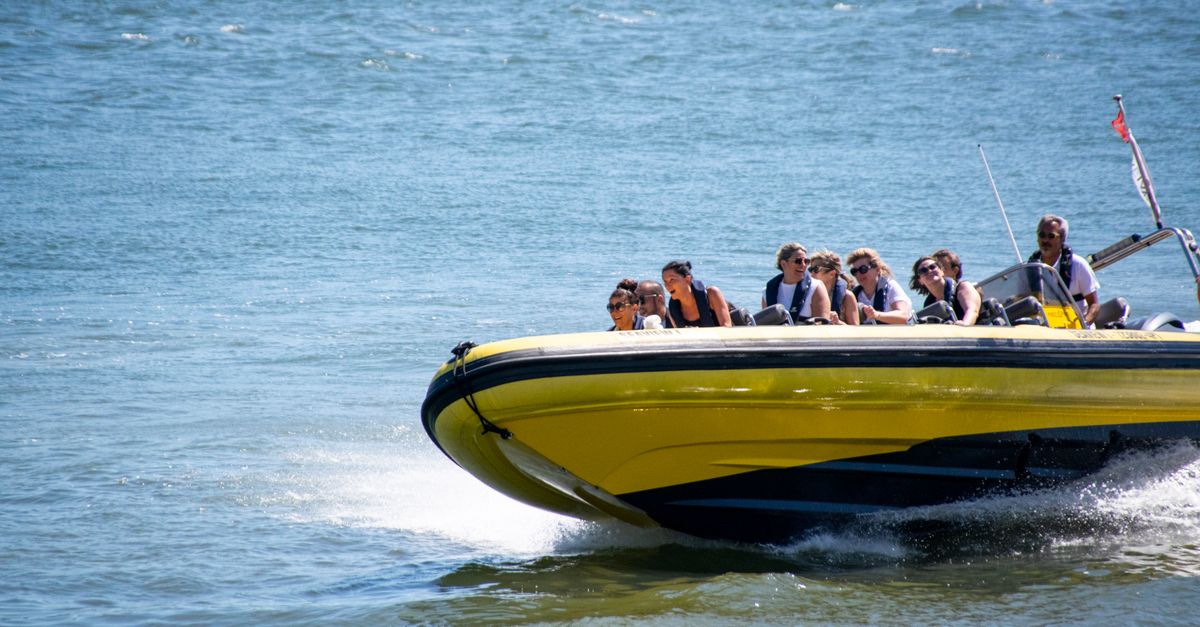 Small motorboat with guests in life jackets in front of yellow limestone cliffs and a cave entrance