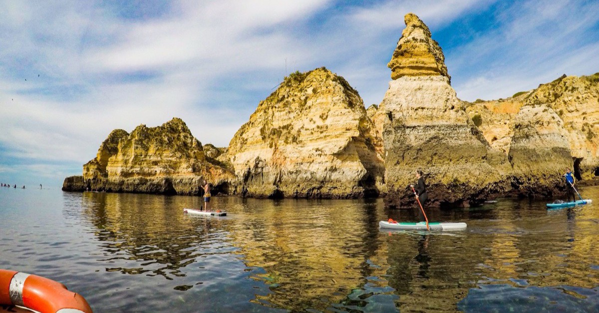 Three paddlers gliding across mirror-flat water in front of yellow sandstone cliffs